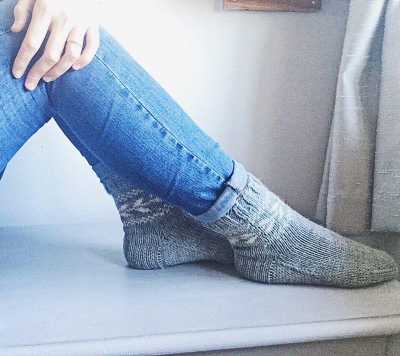 Grey socks with white colour work around the cuffs are shown from the side, modelled with turned up jeans.